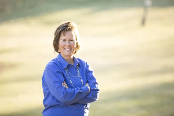 Bitsy Galaska, co-plaintiff in Hartnett v. PSEA, smiling in front of a field in a blue shirt with her arms crossed.