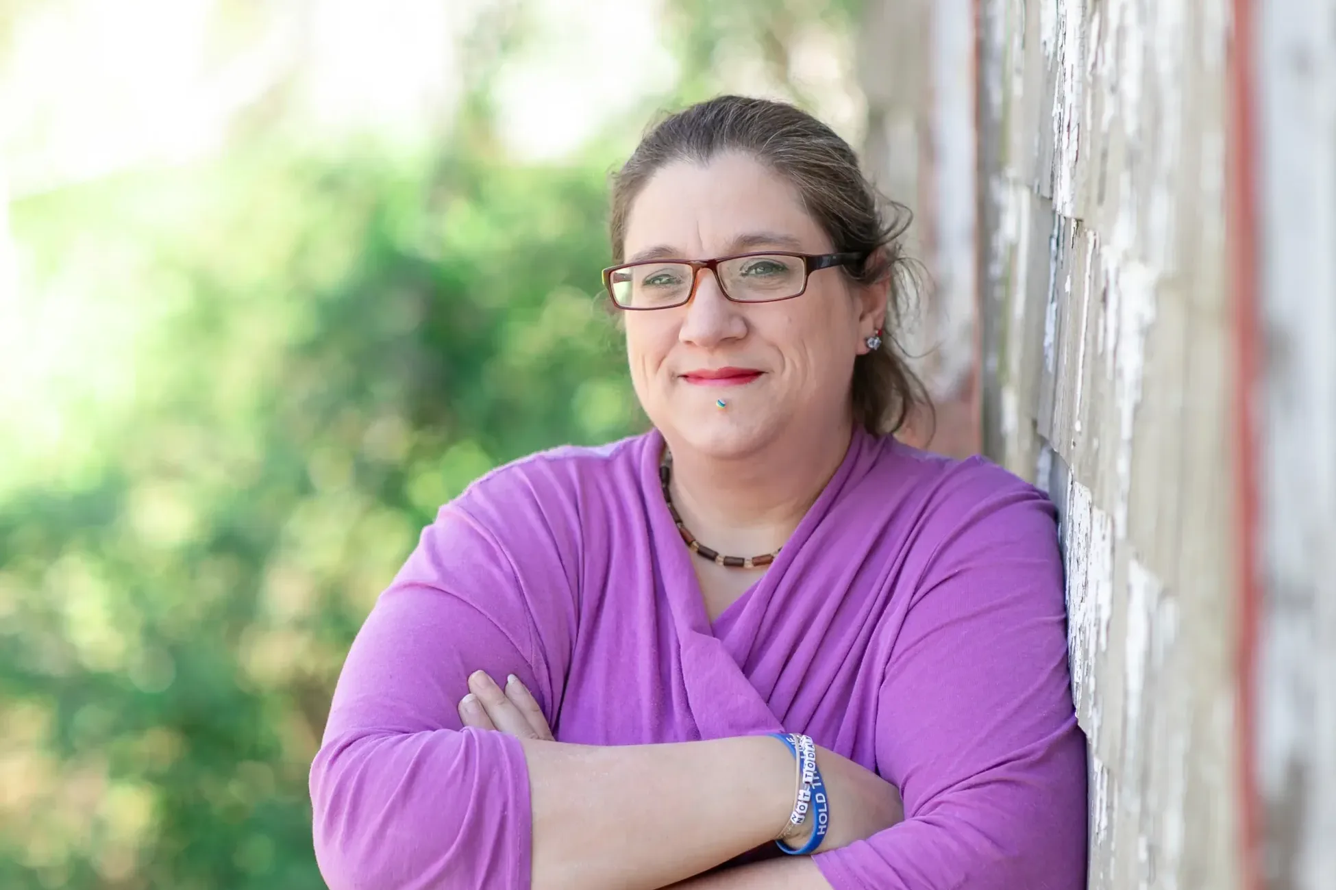 Ashley Kjarbo, plaintiff in Kjarbo v. NETU, IRS, leaning against a weathered wooden shingled house.