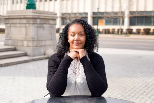 Amber Welch, plaintiff in Welch v. CSEA, Local 100, sitting on a brick-laid sidewalk with her elbows resting on a black marble table.