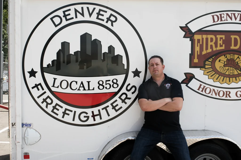 Devin Hallock, secretary-treasurer of Denver Fire Fighters Local 858 poses before a union logo for the lawsuit Denver Fire Fighters Local 858 v. Colorado Professional Fire Fighters & IAFF