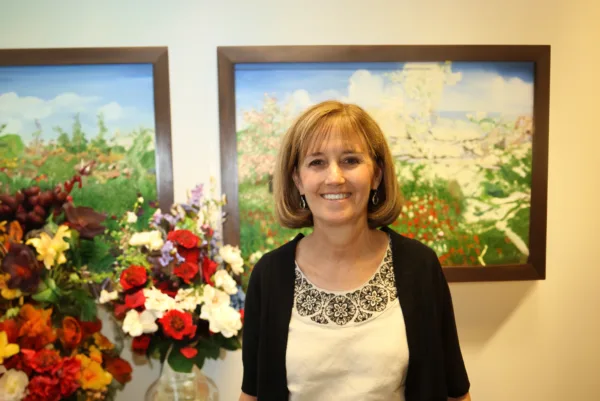 Jane Ladley, lead plaintiff in Ladley v. PSEA, standing in front of framed paintings of flowers with vases of flowers underneath, smiling at the camera.