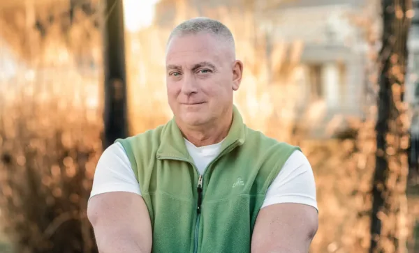 John Grande, plaintiff in Grande v. HFT, smiling in front of a field of tall grasses.