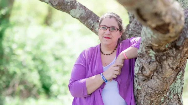 Ashley Kjarbo, plaintiff in Kjarbo v. NETU, IRS, leaning against a tree smiling into the camera.