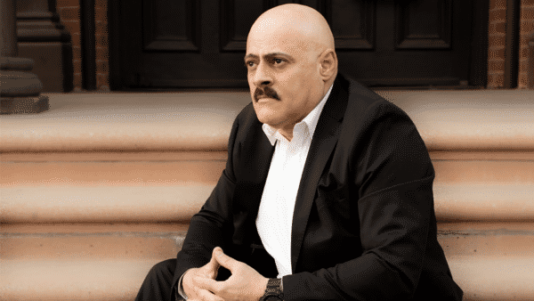 Eddie Mendez, lead plaintiff in Mendez & Garcia v. AFSCME, District Council 37, sitting on steps leading up to a dark wooden door with his hands folded and thumbs pressed together.