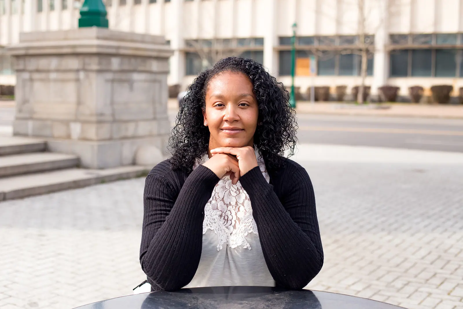 Welch_Hompeage Amber Welch, plaintiff in Welch v. CSEA, Local 100, sitting on a brick-laid sidewalk with her elbows resting on a black marble table.