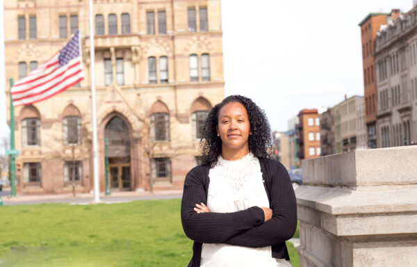 Amber Welch, plaintiff in Welch v. CSEA, Local 100, standing with her arms crossed in front of an old stone building and American flag.