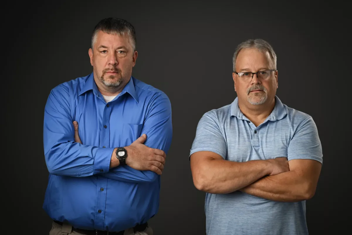 Yedlosky-30 Chris Taylor and Cory Yedlosky, plaintiffs in Taylor v. PSCOA and Yedlosky v. PSCOA, standing with their arms crossed in front of a black background.