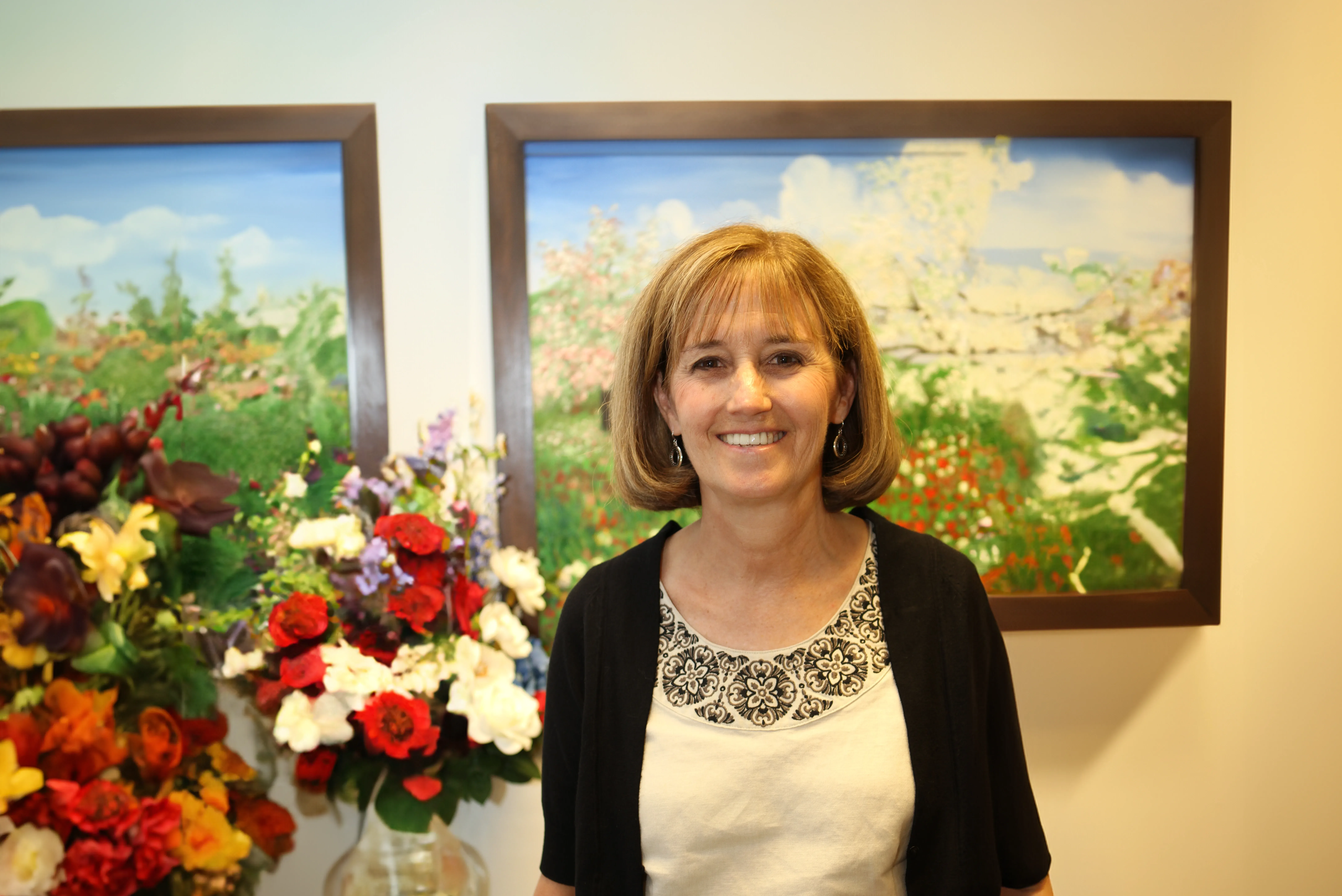 Jane Ladley, lead plaintiff in Ladley v. PSEA, standing in front of framed paintings of flowers with vases of flowers underneath, smiling at the camera.