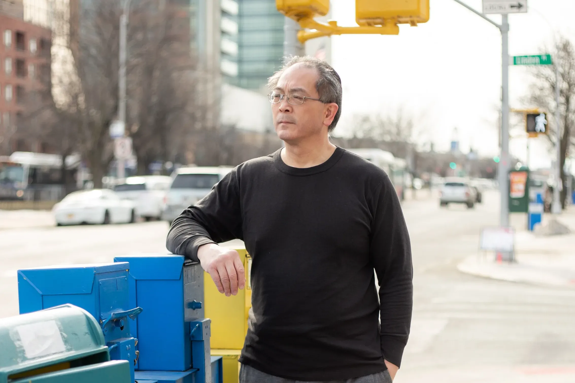 Wayne Wong, plaintiff in Wong v. TWU, Local 100, leaning against newspaper receptacle with New York City behind him.