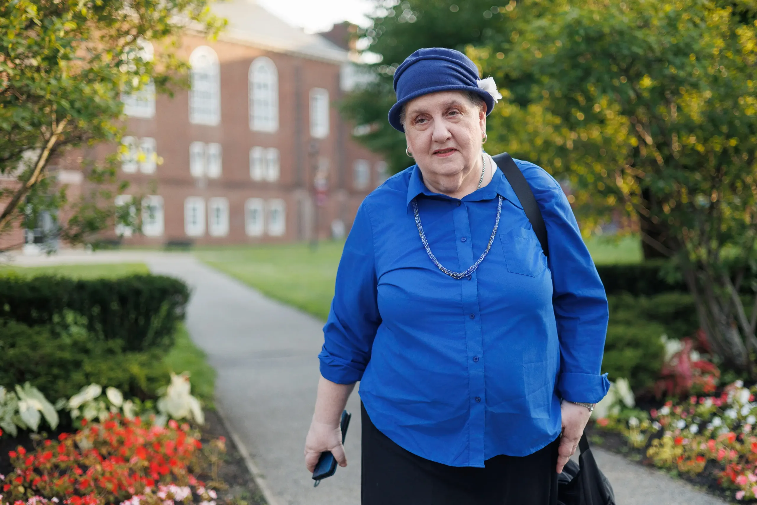 Frimette Kass, plaintiff in Goldstein v. PSC/CUNY, walking down a flower lined path in front of a CUNY building.
