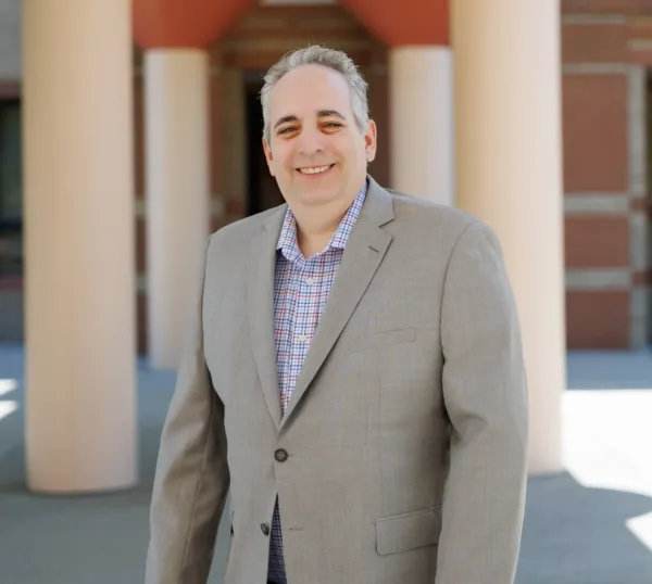 Jeff Lax, plaintiff in Goldstein v. PSC/CUNY, smiling in between pillars leading to the entrance of a CUNY campus building.