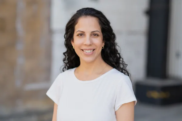 Our client Karin Yaniv, an Israeli postdoc at UC Berkeley suing her union for anti-Semitism, smiling in front of a white and brick building.