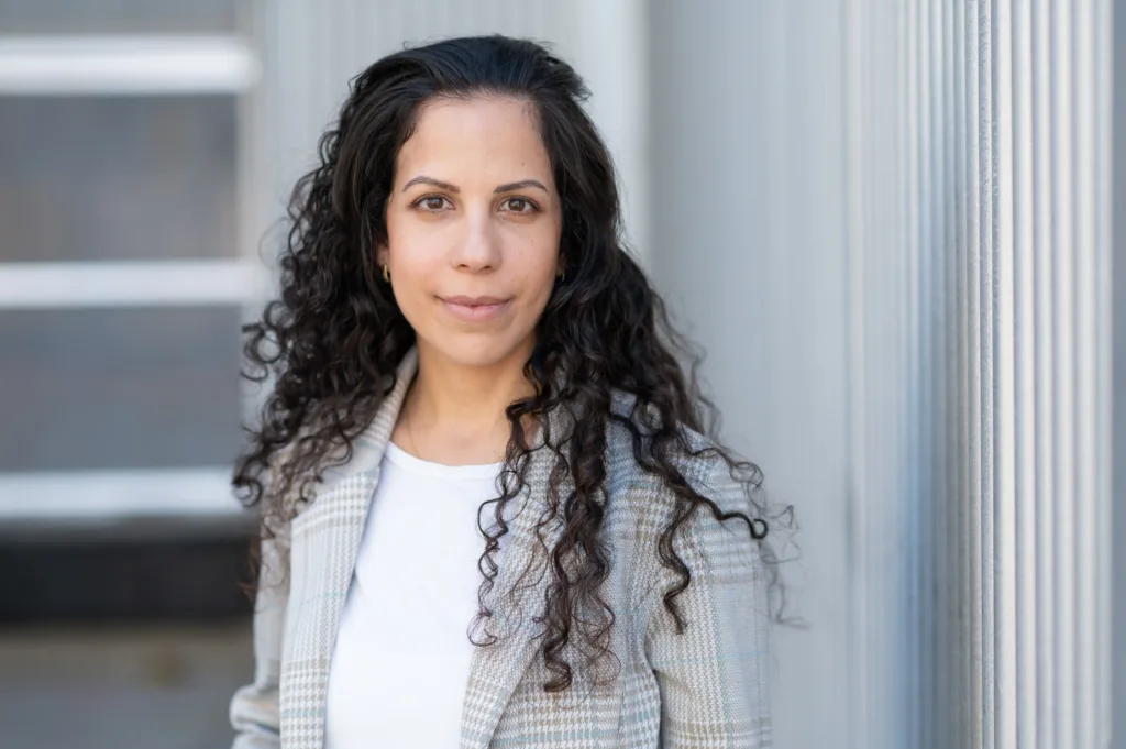Our client Karin Yaniv, an Israeli postdoc at UC Berkeley suing her union for anti-Semitism, smiling against a metal wall.
