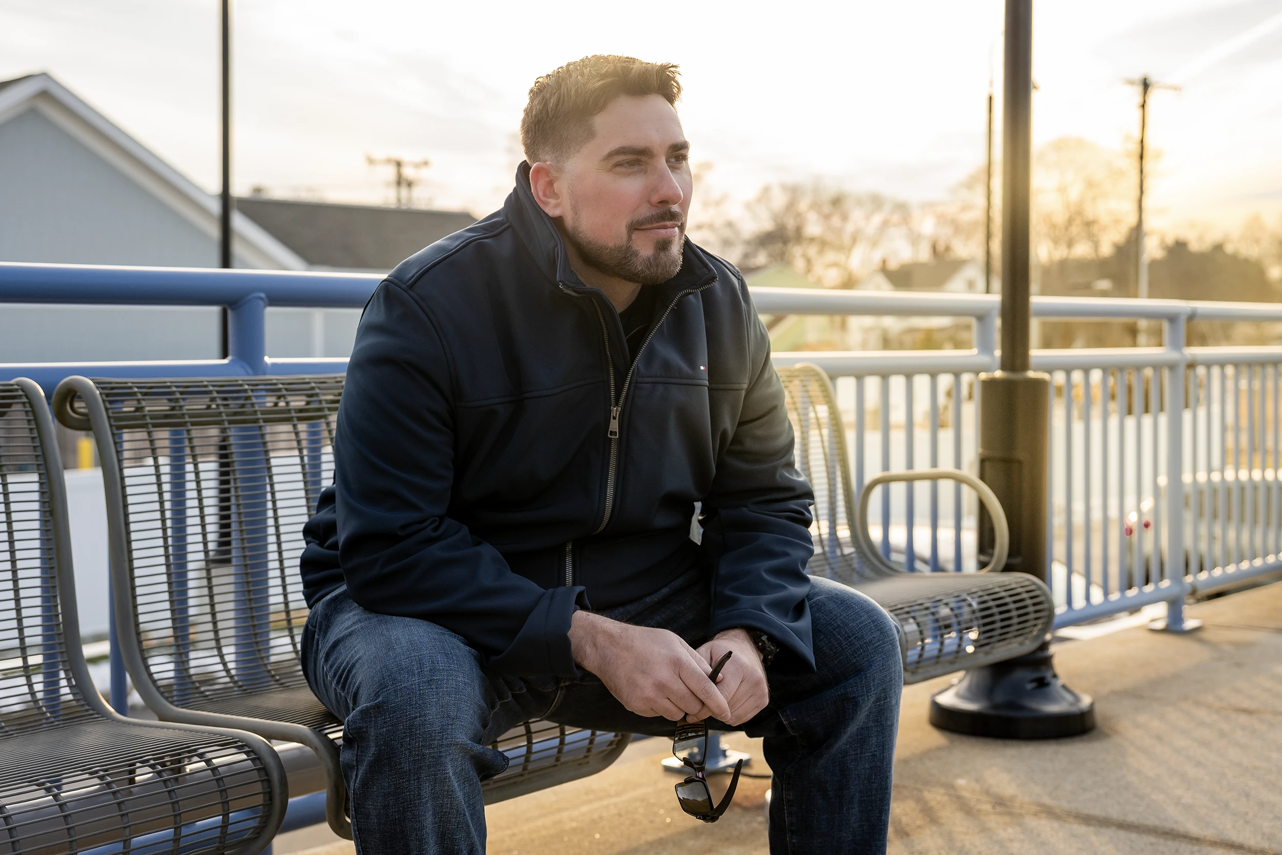 A man, Ryan Bilodeau, in a jacket sitting on a bench near a train station. He is a plaintiff in Bilodeau v. AFSCME Local 391